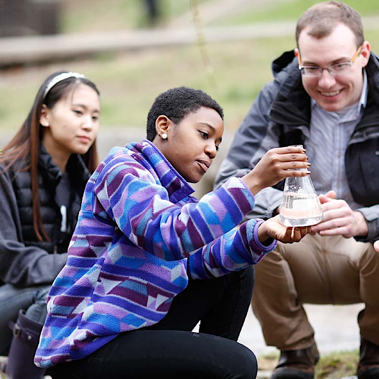 Student look at a beaker while holding class outside. 
